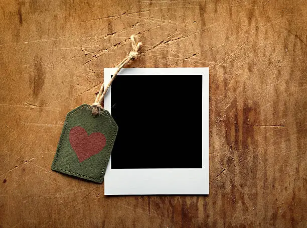 Blank picture frame with gift tag on old vintage wooden background.