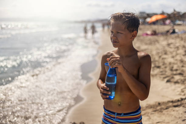 garotinho na praia bebendo de garrafa de água reutilizável. - water child bottle little boys - fotografias e filmes do acervo