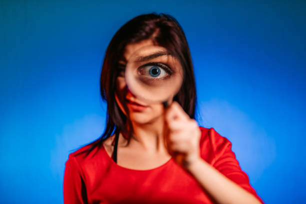 Smiling young woman looking through magnifying glass at camera.