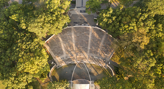 A top down shot directly above a park, located on the edge of the East River in New York City on a sunny Sunday morning. The picture was shot with a drone. In the park there are green landscapes with green trees, it's early in the morning so the park is empty.