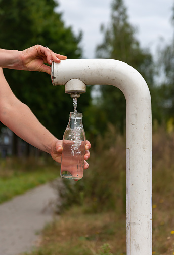 Primer plano de una botella de vidrio rellenada a mano con agua de un grifo público gratuito photo