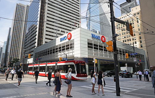 Toronto, Canada - August 30, 2021: Pedestrians cross Bay Street at King Street West intersection. A TTC streetcar heads east through the Bay Street Corridor. Financial institutions line this downtown district. Summer morning in Canada's largest city.