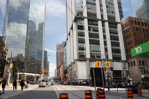 Toronto, Canada - August 30, 2021: Pedestrians walk along Queen Street West near Toronto City Hall on a summer afternoon. Empty streetcar tracks and overhead cables indicate transit service temporarily rerouted with ongoing road work by the traffic cones. Large office buildings line the Bay Street Corridtor in the Financial District.