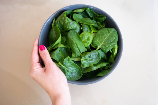 istock Female hand holding bowl with fresh spinach on light background. 1344311898
