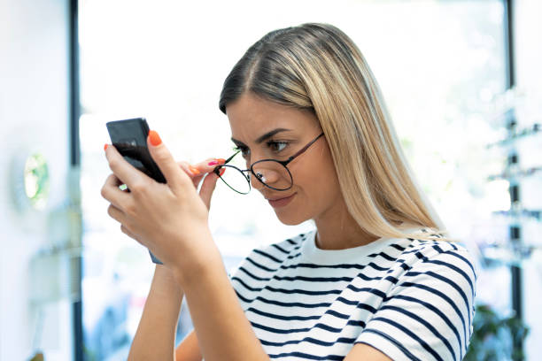 Redhead young woman with eyesight problems trying to read phone text Redhead young woman with eyesight problems trying to read phone text stalker stock pictures, royalty-free photos & images