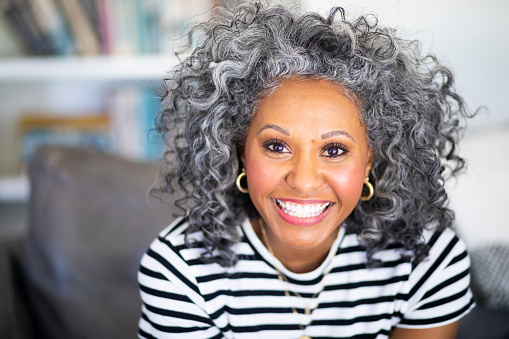 A beautiful black woman with white curly hair  smiles for a headshot