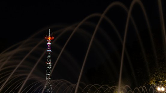 TV Tower in festival illumination. On foreground fountain with long exposure water drop. Minsk Day celebration with bright firework in river.