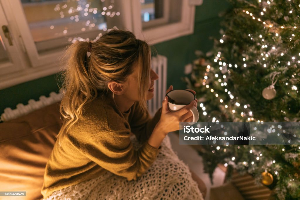 My kind of Christmas Photo of a young woman drinking hot chocolate in the living room of her apartment; enjoying the peaceful Christmas Eve at home alone. Christmas Stock Photo