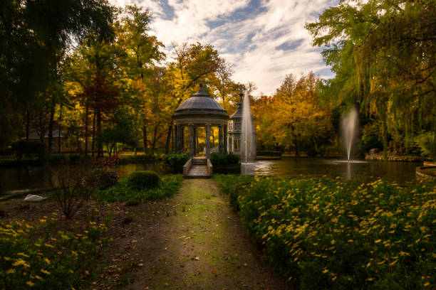 Garden in autumn with lake, fountains and pavilions. Trees with golden, yellow and brown leaves. Garden in autumn with lake, fountains and pavilions. Trees with golden, yellow and brown leaves. In the foreground a path with flowers and in the background trees and sky with clouds. Autumn Concept aranjuez stock pictures, royalty-free photos & images