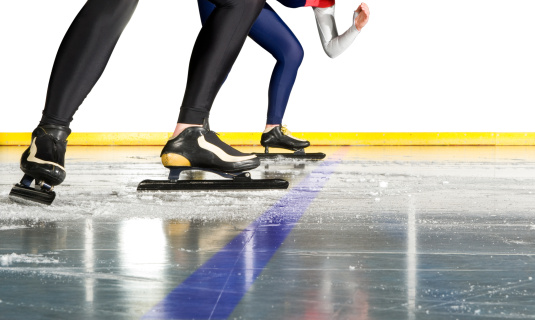 Two female speed skaters taking starting positions on the ice behind the starting line