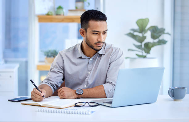 istock Shot of a young businessman writing notes while working on a laptop in an office 1344323402