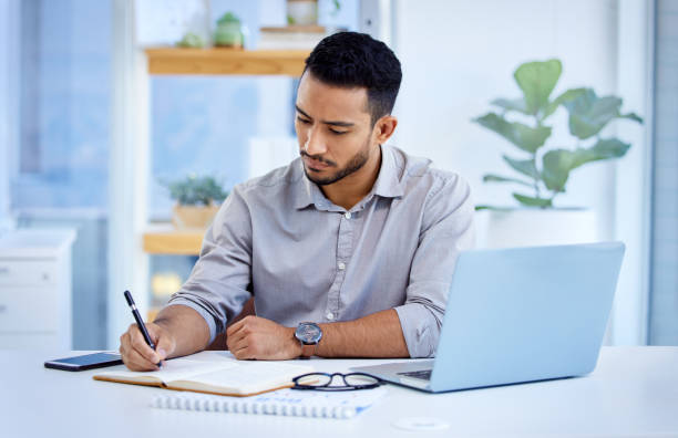 istock Shot of a young businessman writing notes while working on a laptop in an office 1344323409