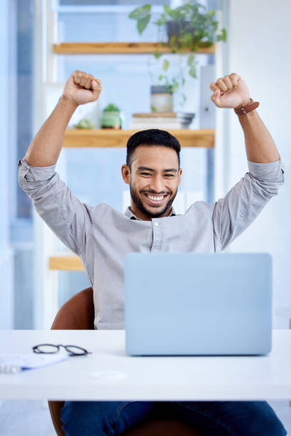 shot of a young businessman cheering while working on a laptop in an office - excitement business person ecstatic passion imagens e fotografias de stock