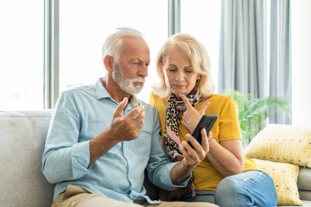 besorgtes älteres paar, das schlechte nachrichten am telefon liest. - couple senior adult sadness emotional stress stock-fotos und bilder