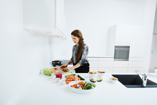 Cooking vegan food in white and bright modern kitchen. Real people making a lunch of raw food
