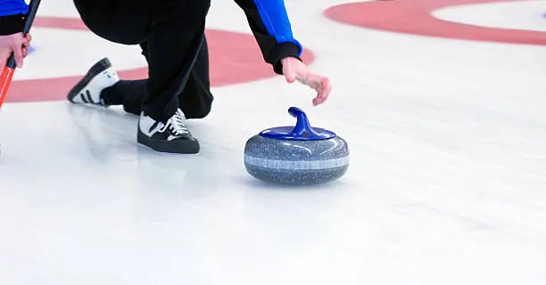 Curling player delivering a stone on a curling rink, sliding over the ice