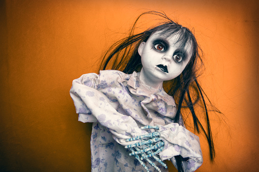 A close up of a creepy doll Halloween decoration on a dirty orange background.