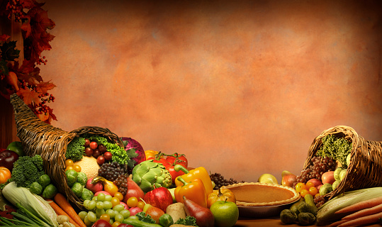 A Thanksgiving cornucopia of fruits and vegetables rests on a table in front of an old world painted background.