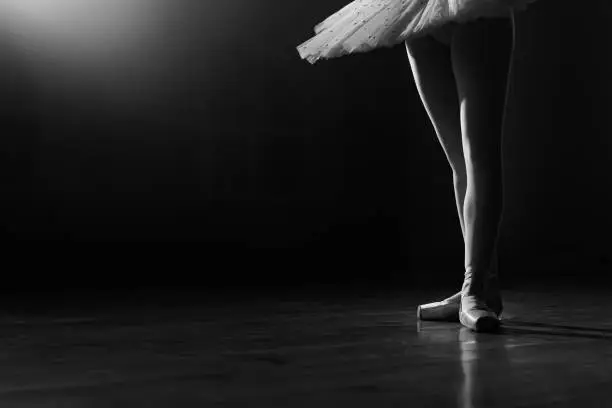 Ballet dancer's legs in pointe shoes on theater stage. Ballerina standing in 3 third position on black and white background. Beautiful woman's feet. Lady shows classic pas. High quality photo