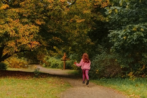 A girl with red hair runs away in an autumn park in the afternoon.