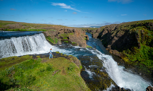 Tourist standing at the edge of Rejkjafoss waterfall on river  Huseyjarkvisl, North Iceland. Shi is looking and enjoying it as it is cascade, two big steps waterfall.