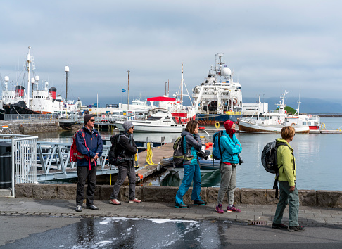 Tourists at old harbor in Reykjavik,  capital of Iceland.  In background are boats and fisherman ships, above cloudy sky.