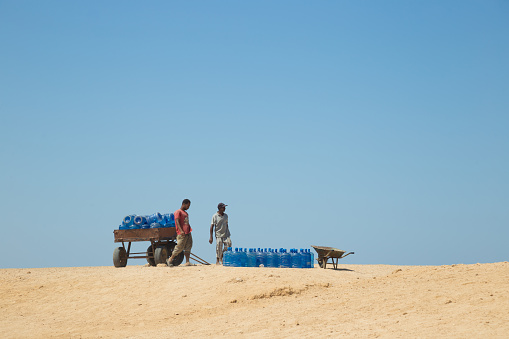 Paradise Beach, Big Giftun, Red Sea, Egypt - August 23, 2021: Two man bringing water supply for beach cafe on the island. Hard work on hot African sun.