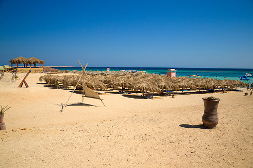 Paradise Beach, Big Giftun, Red Sea, Egypt - August 23, 2021: Sandy beach with tourists under sunscreens made out of palm leaves.