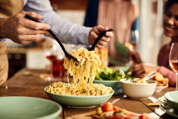 Close-up of man serving pasta at dining table.