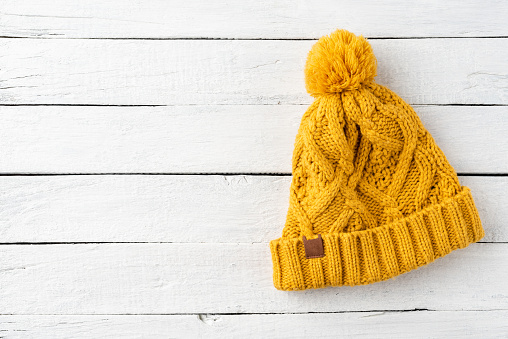 Yellow knitted hat on white wooden background with copyspace. Top view