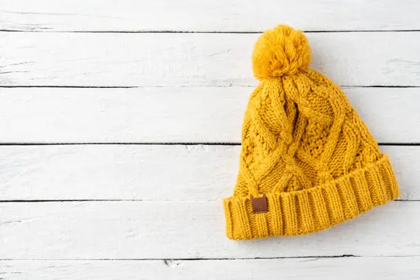 Photo of Yellow knitted hat on white wooden background with copyspace. Top view