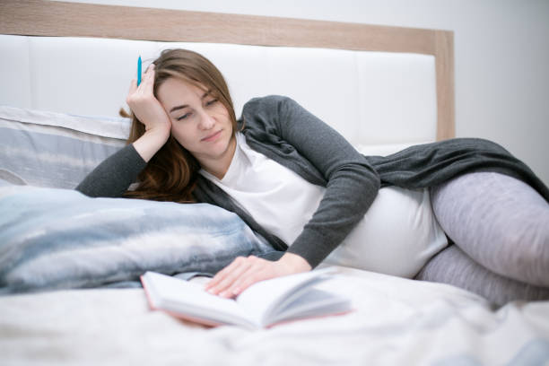 istock Beautiful pregnant woman laying down on a bed with a notepad. 1344375320