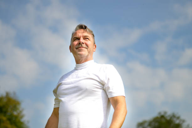 Low angle view against sky of a fit pensive senior man in sportswear standing looking to the side with a thoughtful expression with copyspace