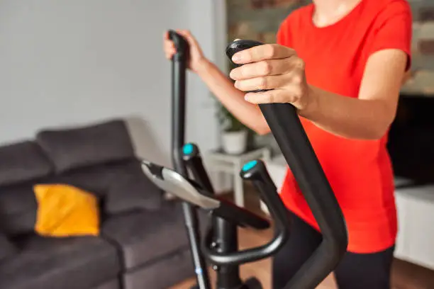 Unrecognizable woman at home training on smart elliptical trainer indoors in daylight with natural light