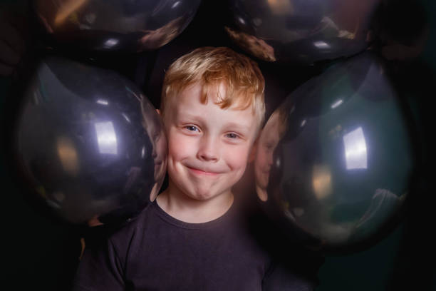 carino divertente baby boy europeo è circondato da palloncini neri. primo piano del viso. il ragazzo sorride. - child balloon selling sign foto e immagini stock