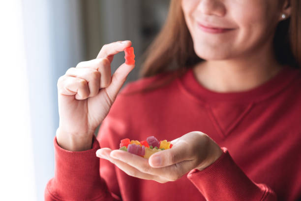 nahaufnahme einer jungen frau, die einen roten gummibärchen hält und betrachtet - gummibärchen stock-fotos und bilder