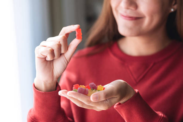 Closeup image of a young woman holding and looking at a red jelly gummy bear stock photo