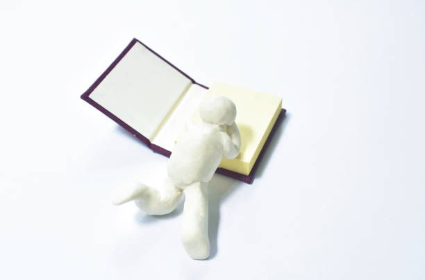 istock clay man lay down reading book with blue cover on white background 1344397072