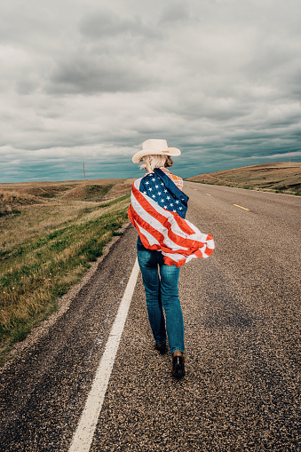 Rear view of a mature woman with an american flag blowing in the wind over her shoulder. Montana wilderness.