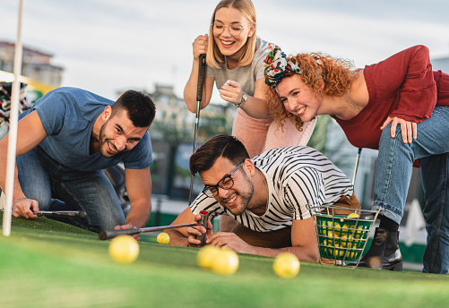 Group of smiling friends enjoying together playing mini golf in the city.