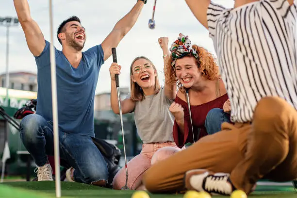 Group of smiling friends enjoying together playing mini golf in the city.