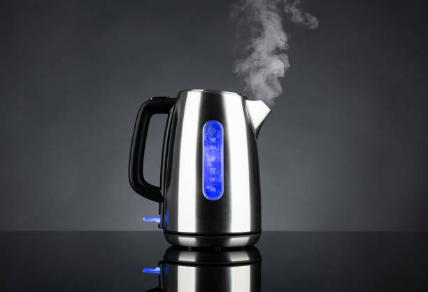istock Boiling steel electric kettle with light and steam with reflection, on black background 1344410027