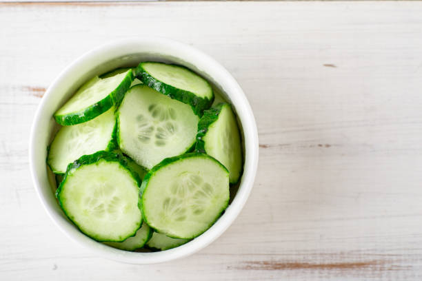 istock Sliced cucumber in a bowl on a white wooden background. 1344410774