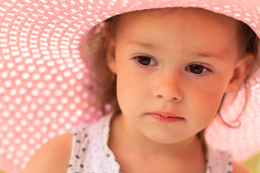 Face of a little cute girl 1-3 in a pink summer wide-brimmed hat in summer