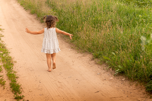 Little cute girl 1-3 in a light dress running on a path in the field on a background of grass in summer