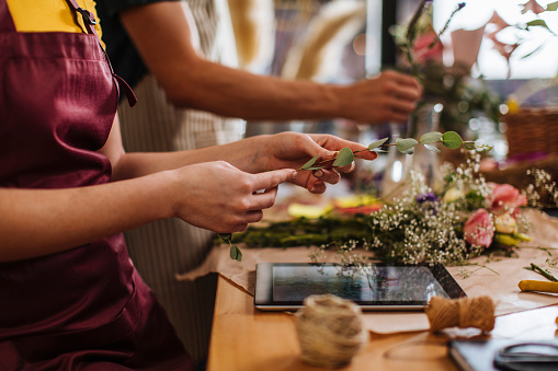 Unrecognizable people arranging a bouquet while also using a digital tablet