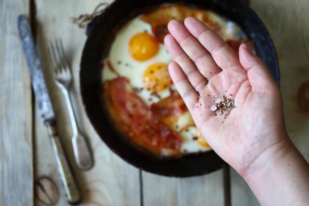 istock Spices in hand. Scrambled eggs bacon in a frying pan on a wooden surface. 1344412880