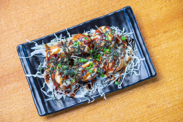 Octopus Fillet Takoyaki Garnish with seaweed. chopped white cabbage and scallions in a black dish, Saimoden, circled on a wooden table Octopus Fillet Takoyaki Garnish with seaweed. chopped white cabbage and scallions in a black dish, Saimoden, circled on a wooden table takoyaki photos stock pictures, royalty-free photos & images