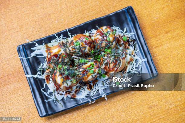 Octopus Fillet Takoyaki Garnish With Seaweed Chopped White Cabbage And Scallions In A Black Dish Saimoden Circled On A Wooden Table Stock Photo - Download Image Now