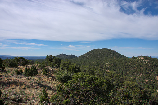 Horizontal high angle landscape of plains, forested hills and white clouds in a blue sky in Summer near Santa Fe, New Mexico.